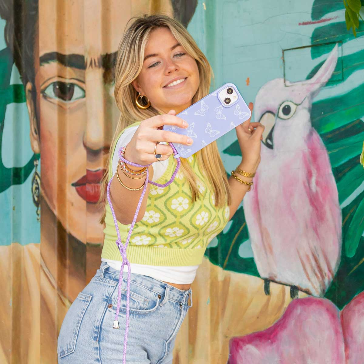 Jonge vrouw maakt selfie voor muurschildering met Frida Kahlo en papegaai.