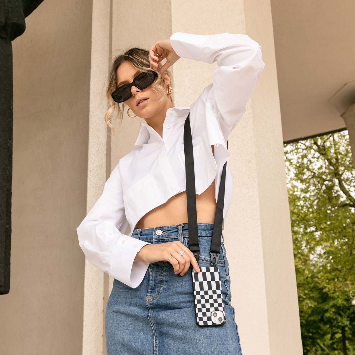 Une femme en lunettes de soleil portant un crop top blanc et un jean. Elle a un étui de téléphone.