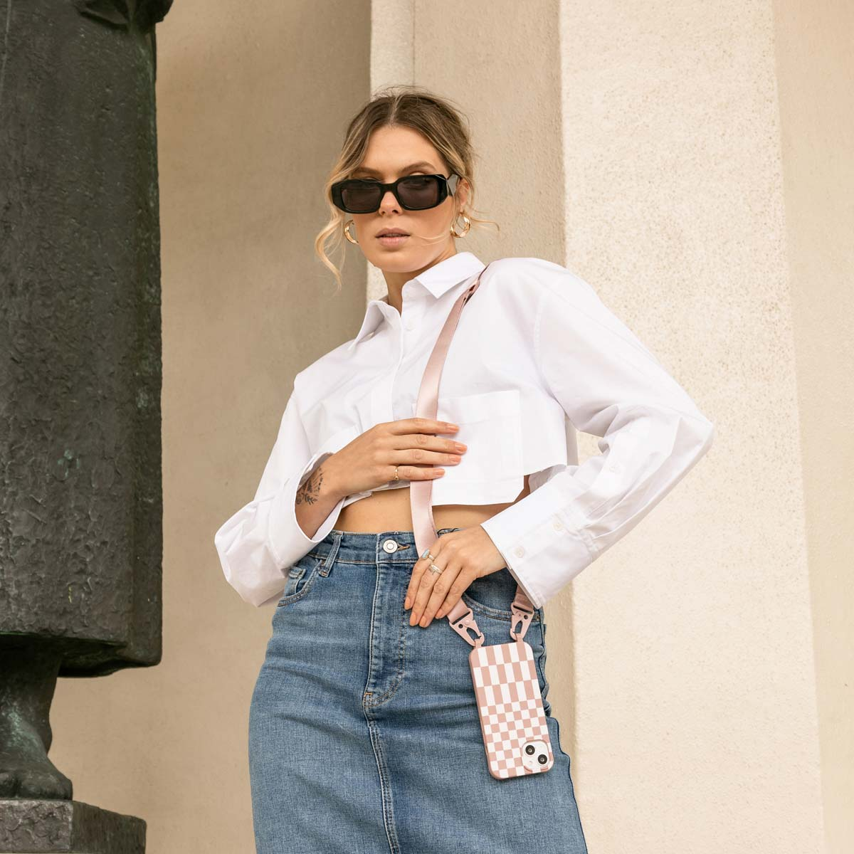 Une femme en lunettes de soleil portant un haut blanc et un jean. Elle a un étui de téléphone.