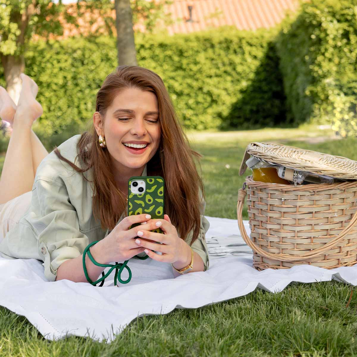 Eine Frau liegt auf einer Decke im Gras und lächelt in ihr Handy. Daneben steht ein Picknickkorb.