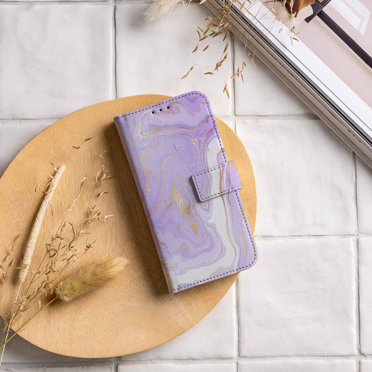 Paarse marmeren telefoonhoes op houten bord, met droge planten en een tijdschrift op de achtergrond.