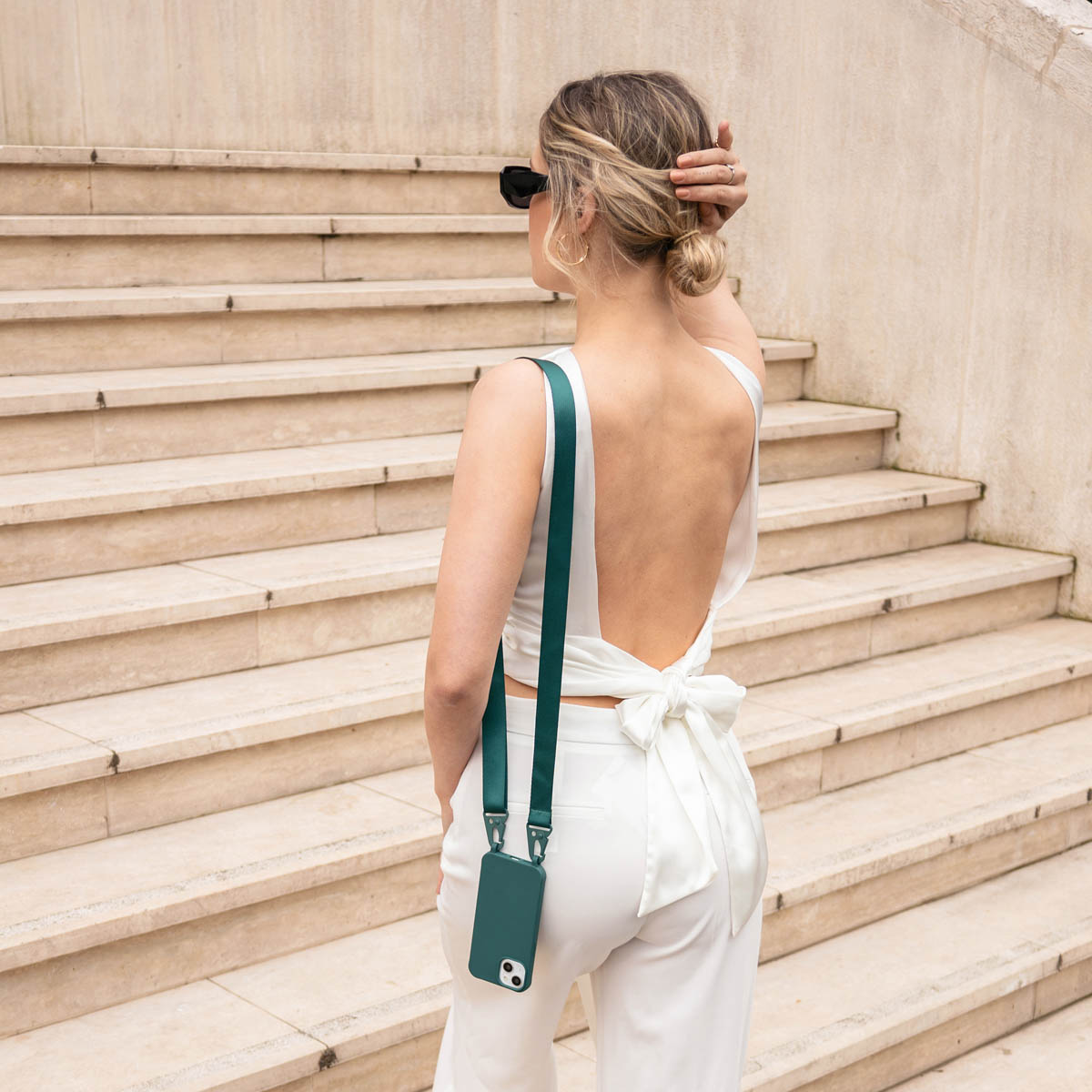 Vrouw van achteren, witte outfit met groene telefoonriem. Trappen op de achtergrond.