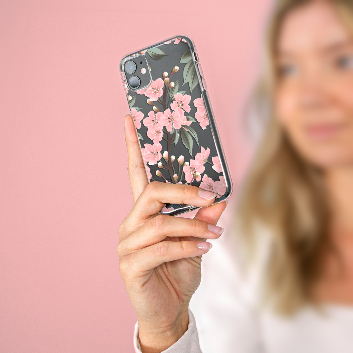 Hand van een vrouw die een doorzichtige telefoonhoes met een bloemenontwerp vasthoudt voor een roze achtergrond.