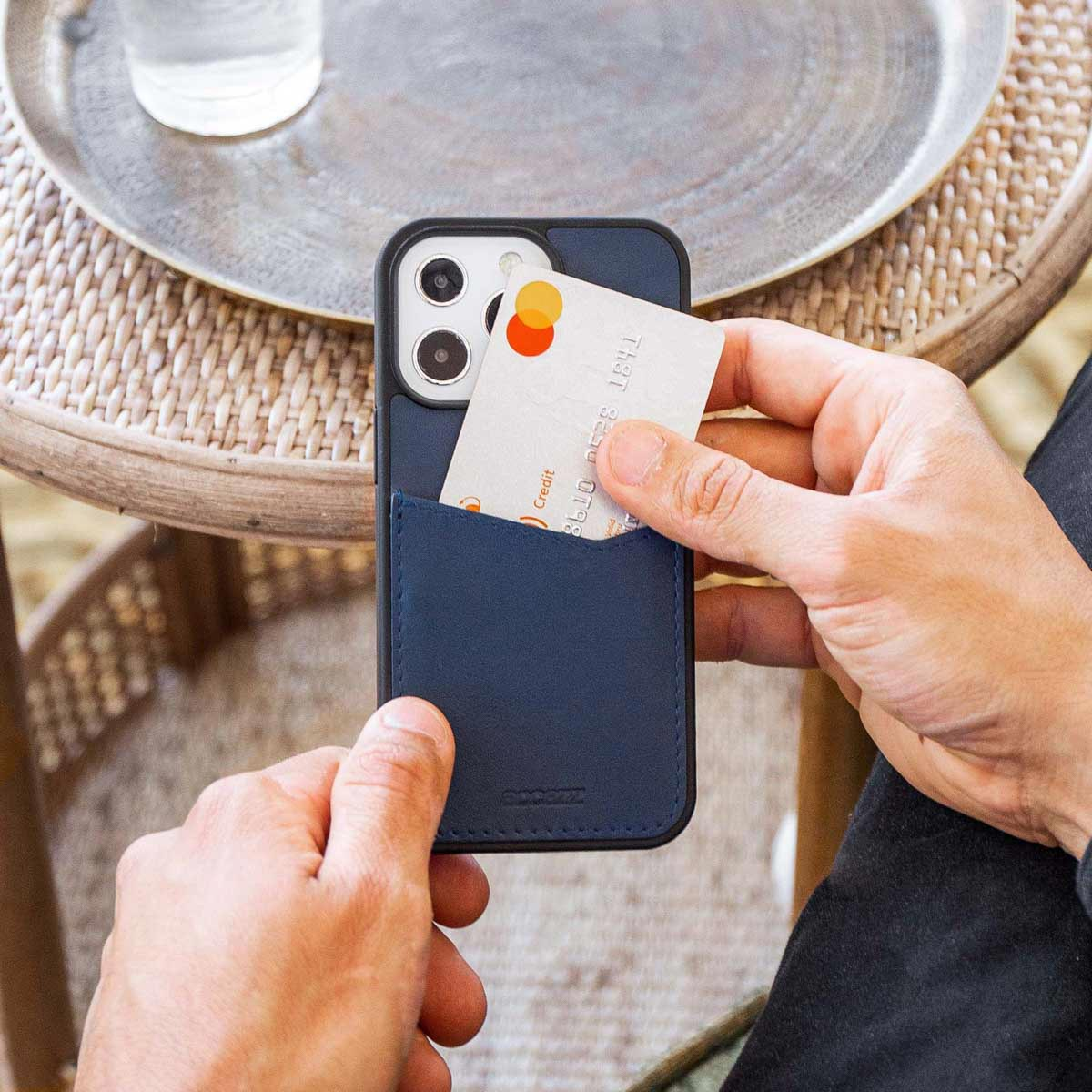 Mains tenant un téléphone avec un étui bleu et une carte de crédit dans la poche.
