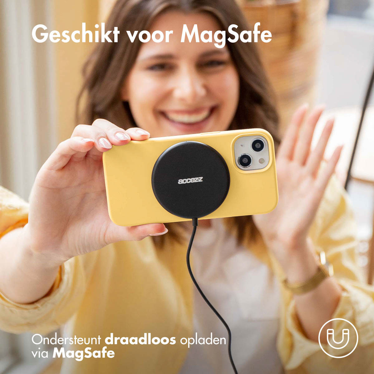 Vrouw die een gele telefoon vasthoudt met een zwarte MagSafe-oplader. De telefoon is geel. Tekst: Ondersteunt draadloos opladen.
