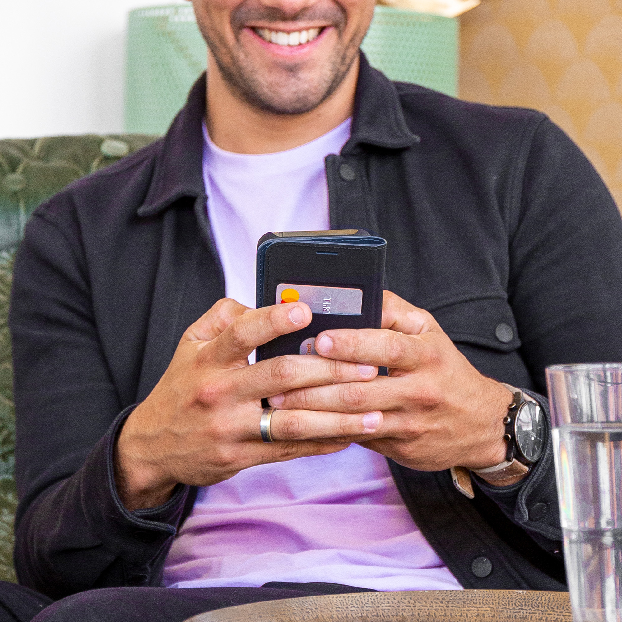 Mann hält ein Telefon mit Kartenetui, sitzt in einem Café.