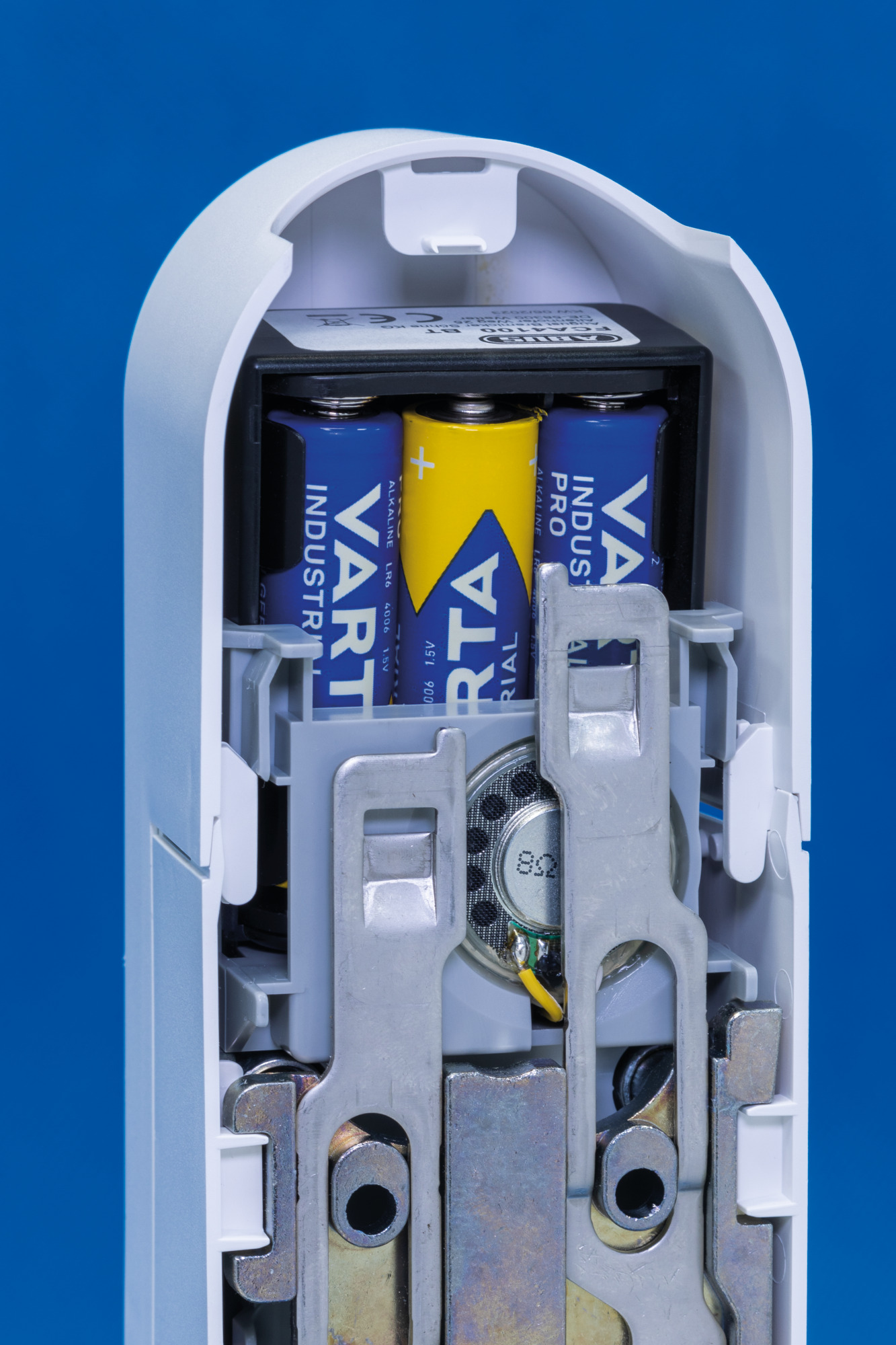 Ein offenes weißes Gerät, das ein Batteriefach mit Batterien zeigt. Ein Lautsprecher ist ebenfalls sichtbar.
