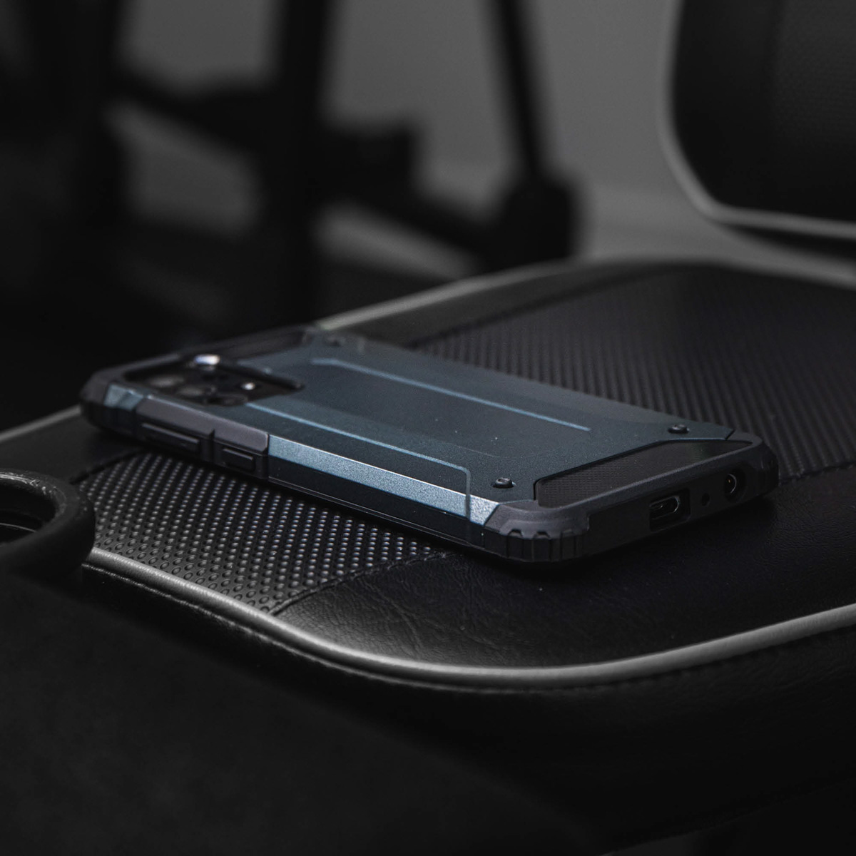 Coque de téléphone noire avec un téléphone sur une chaise en cuir noir. La coque a un design robuste.