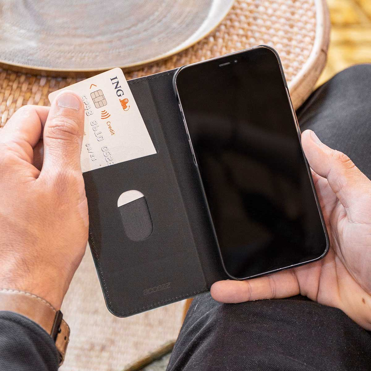 Une personne tient un étui de téléphone avec une carte à l'intérieur, devant un arrière-plan flou. L'étui est noir.