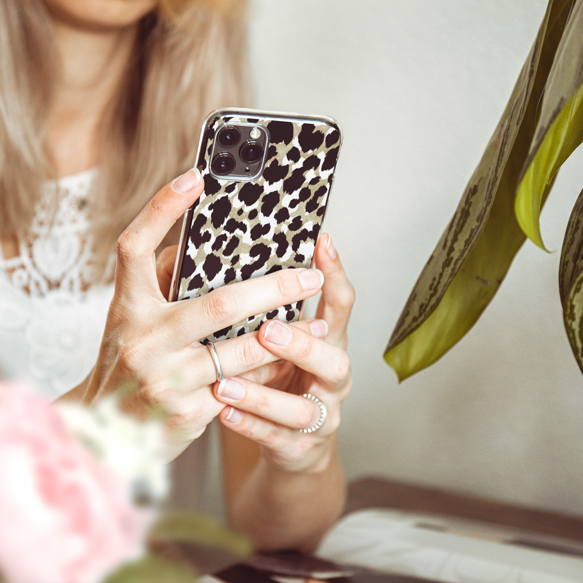 Une personne tenant un téléphone avec un étui à imprimé léopard. L'arrière-plan a une plante.