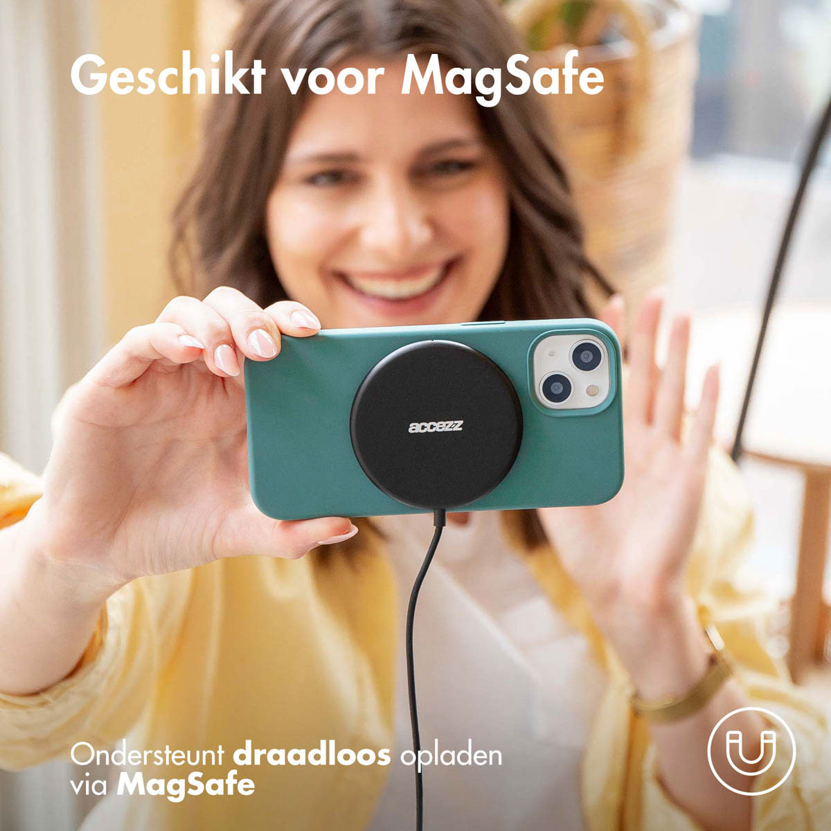 Eine Frau hält ein türkisfarbenes Telefon in einer grünen Hülle mit einem schwarzen MagSafe-Ladegerät.