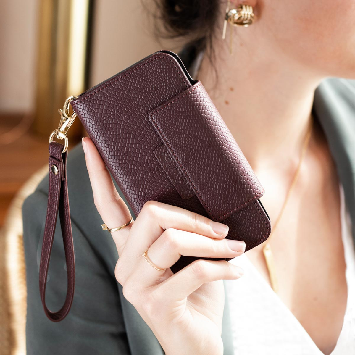 Vrouw houdt donkerpaarse telefoonhoes vast. Ze draagt gouden ringen en een witte top.
