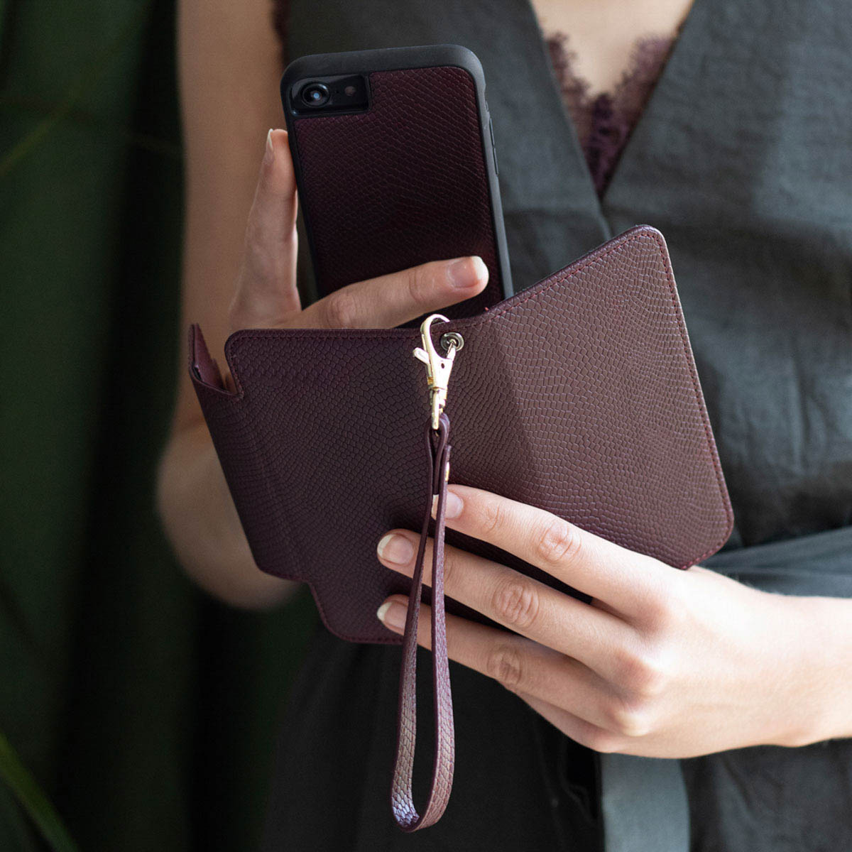Vrouw die een telefoon en een bordeauxrode telefoonportemonnee vasthoudt. Toont de telefoon in en uit de portemonnee.
