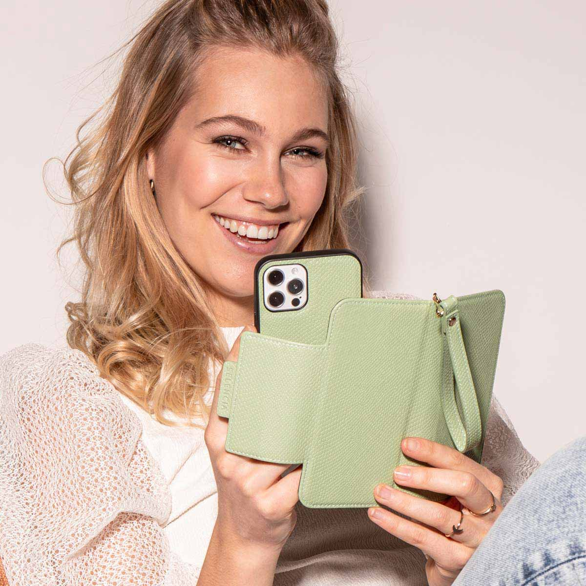 Een vrouw glimlacht en houdt een telefoon vast in een groene hoes, een deel van een groene wallet-hoes is zichtbaar.