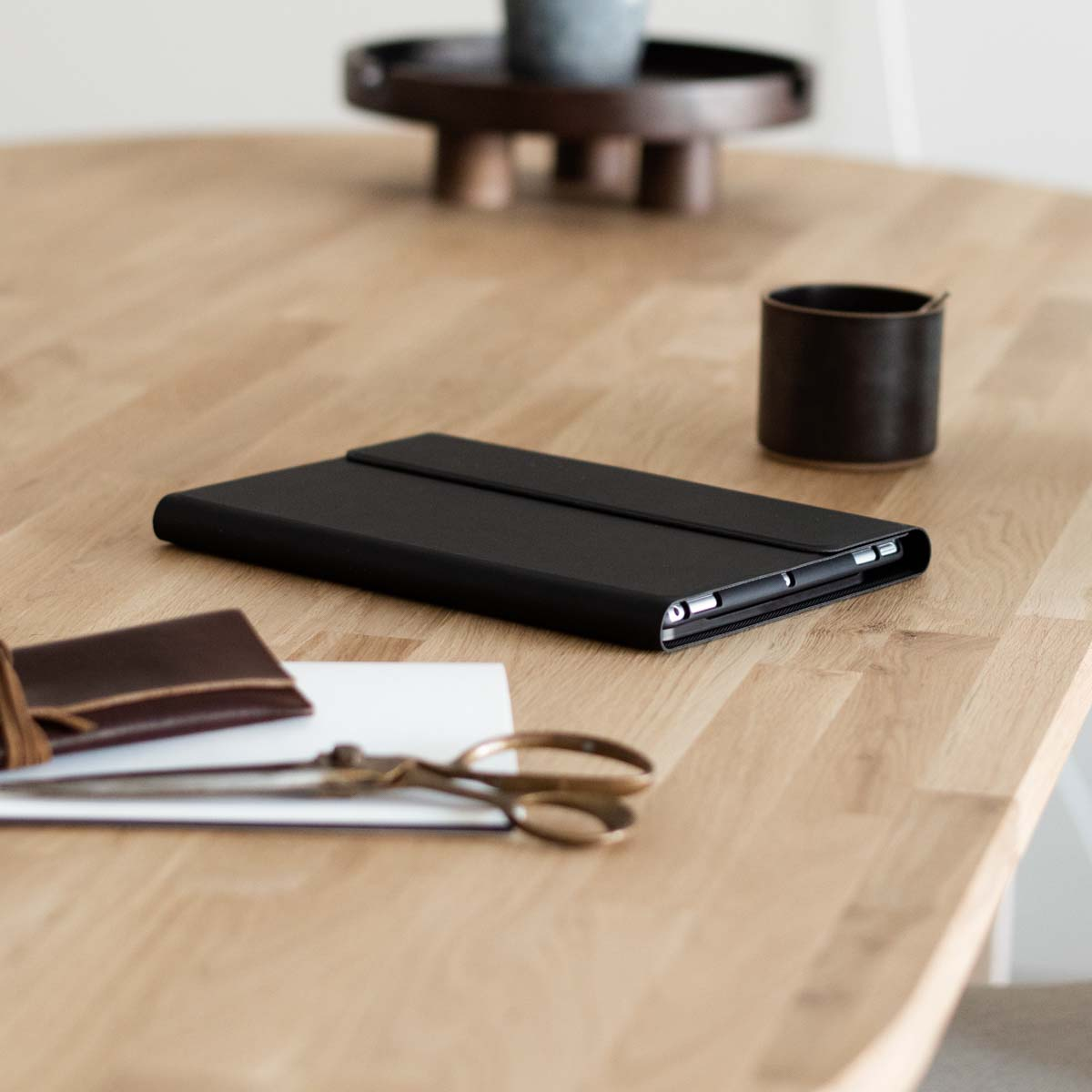 A black phone case and other office supplies on a wooden table. Soft focus.
