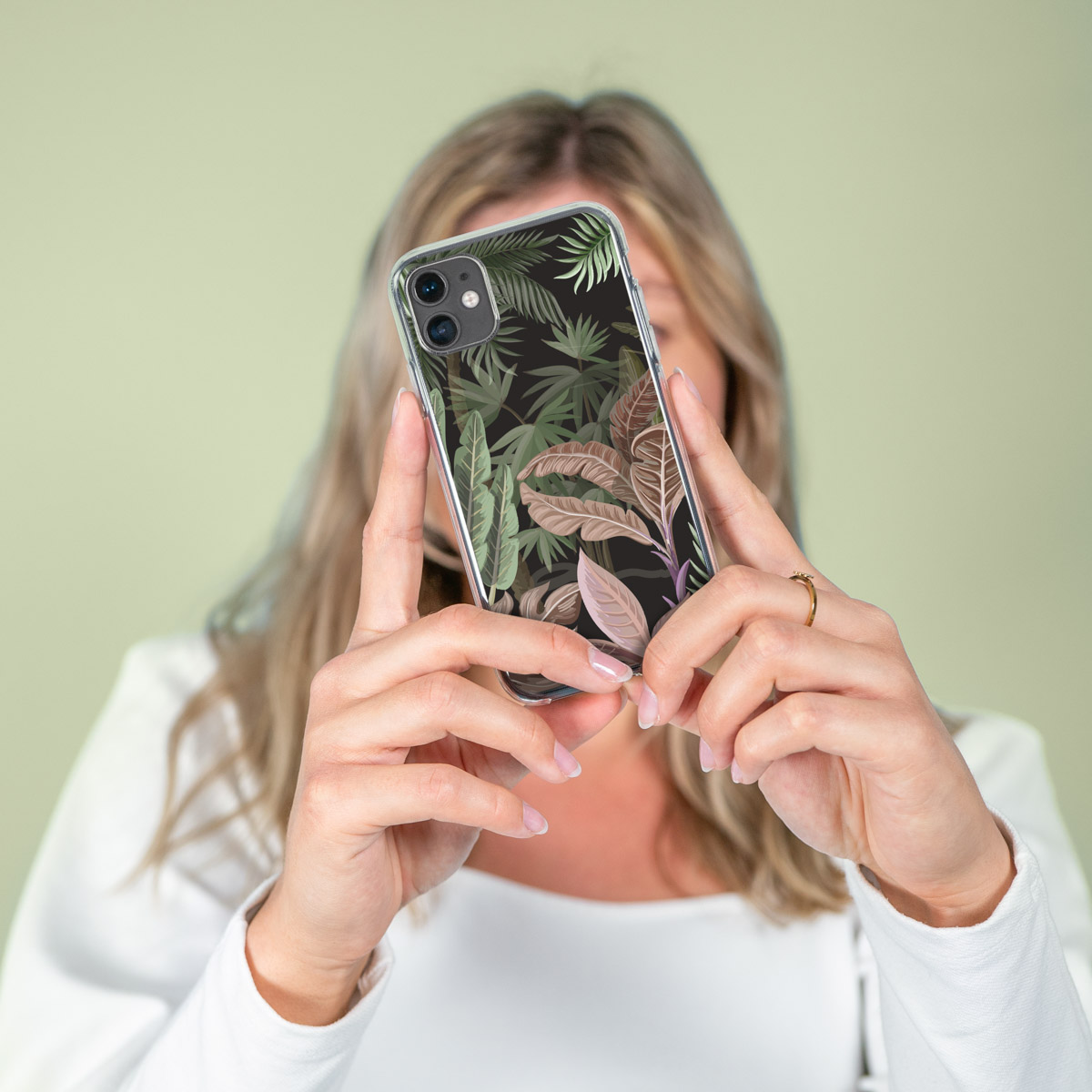 Vrouw houdt een telefoon vast met een hoesje. De hoes heeft een bloemmotief met groene en bruine bladeren.