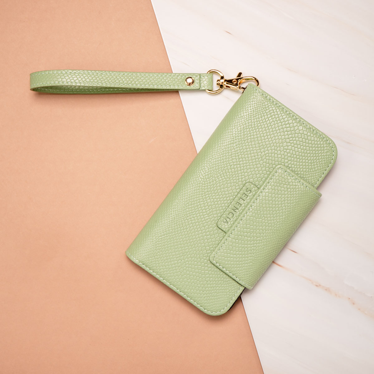Mintgroene portemonnee telefoonhoes met een handvat. Het ligt op een marmeren en roze oppervlak.
