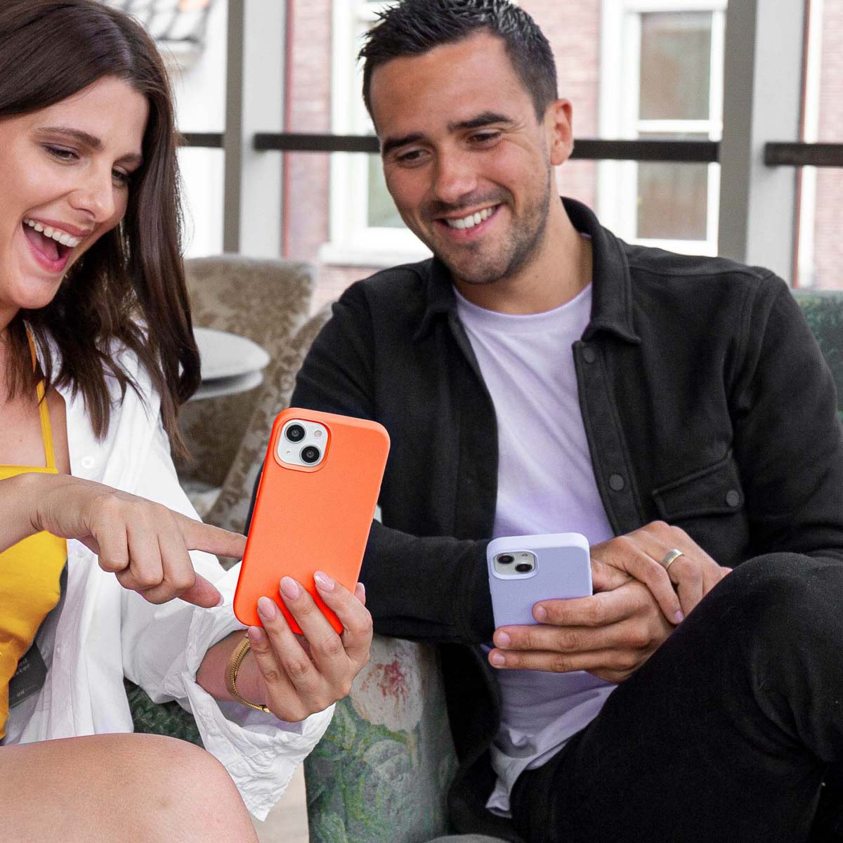 Een man en vrouw houden oranje en paarse telefoons vast, glimlachen en wijzen ernaar.