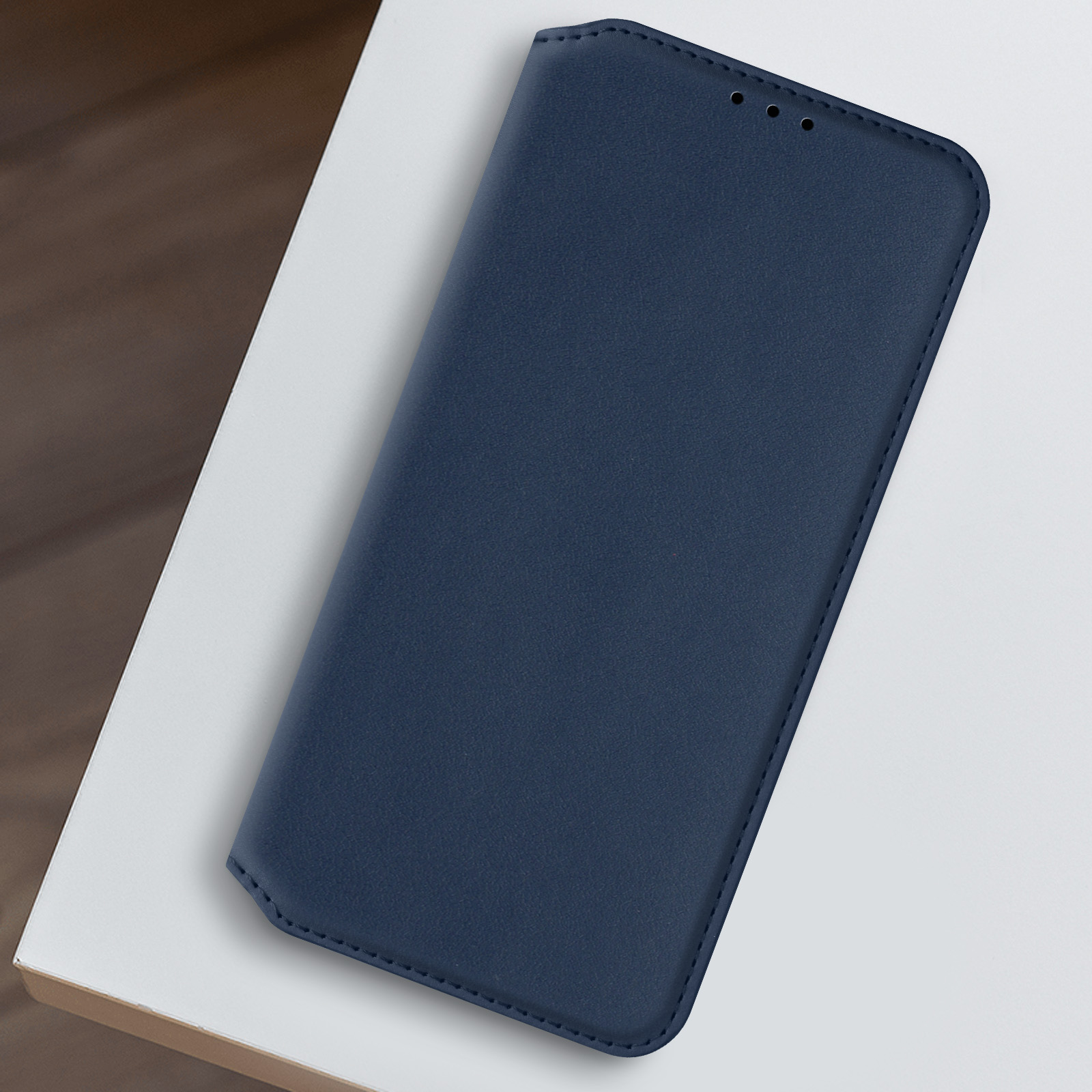 Una custodia per telefono blu navy su una superficie bianca. Lo sfondo è un tavolo di legno.