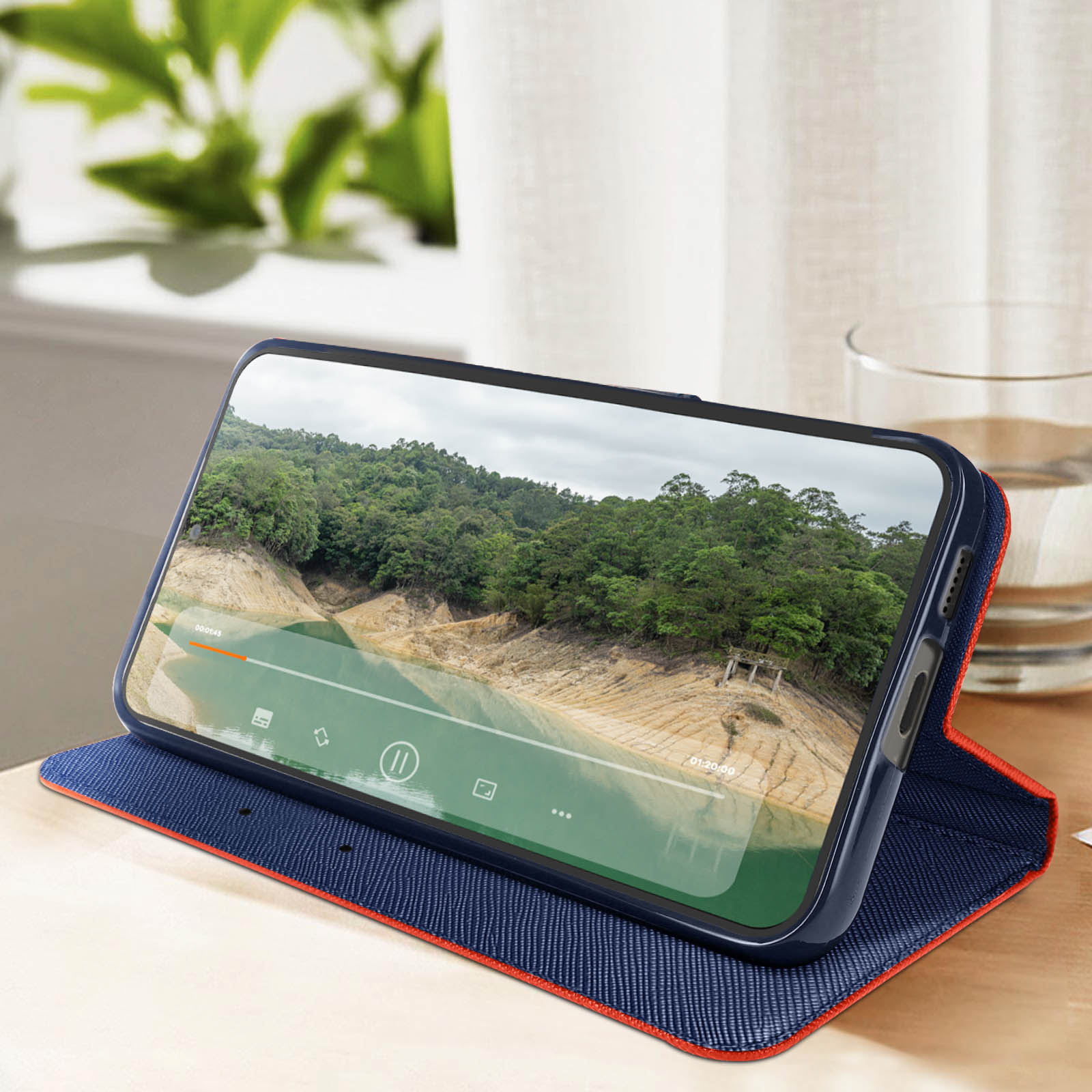 Telefono in una custodia che mostra un video di un lago. La custodia è su un tavolo con un bicchiere d'acqua.