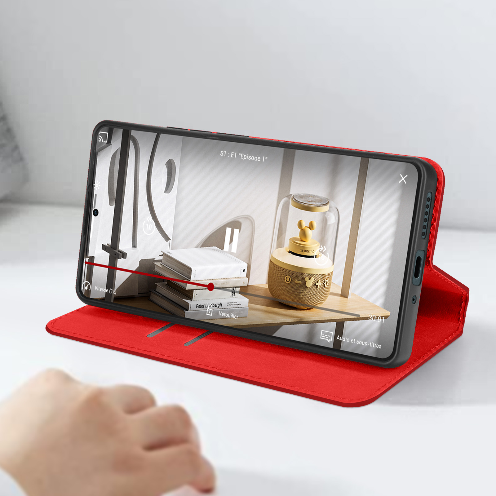 Telefono in una custodia rossa che mostra un video su una superficie di legno.