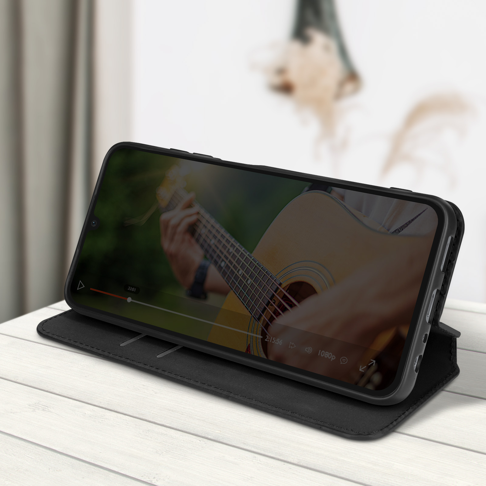 Telefono nero con custodia che mostra un video di chitarra su un tavolo di legno bianco.