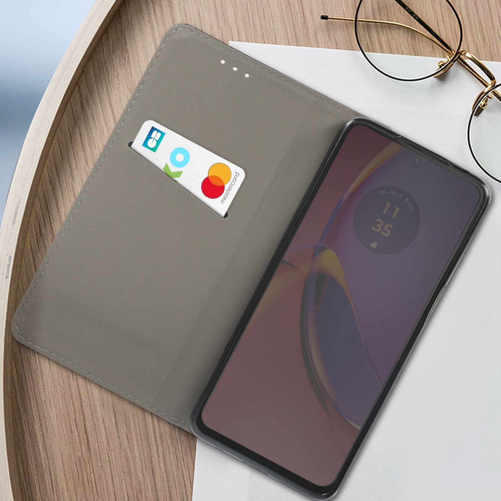 Telefono in custodia a libro grigia con carta e carta di credito. La custodia è su un vassoio di legno.