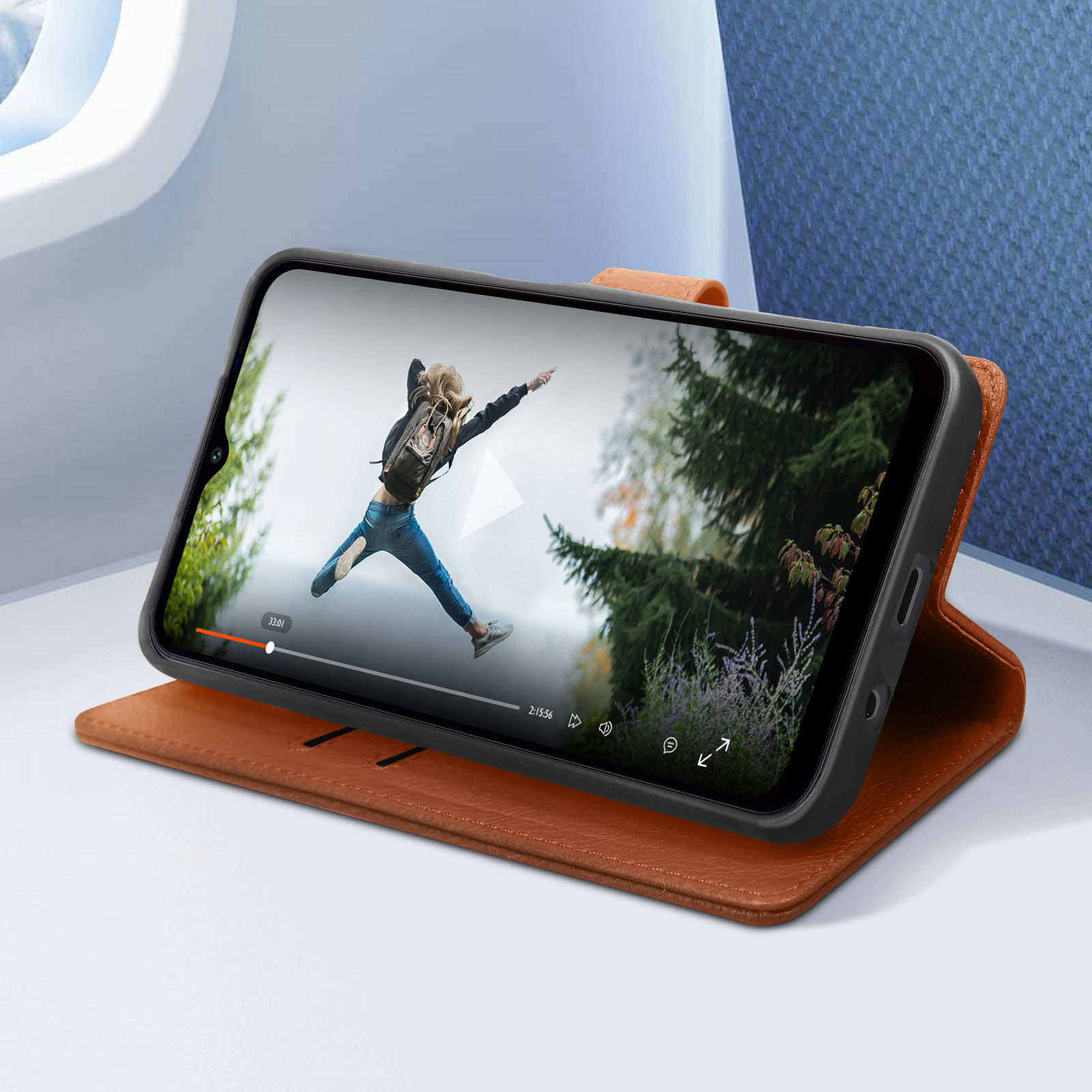 Teléfono en funda de cuero marrón, muestra video de persona saltando. Fondo: interior de avión.