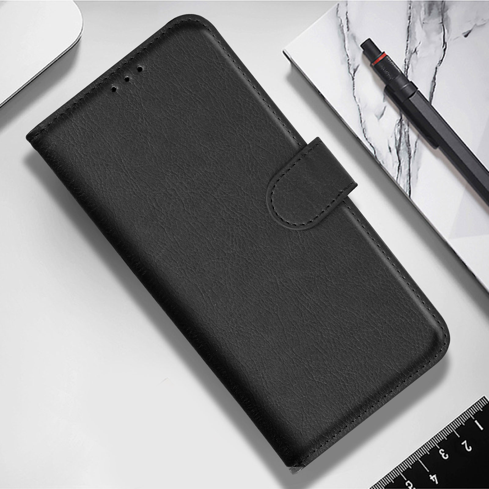 Funda de teléfono de cuero negro sobre superficie blanca, con bolígrafo y regla cerca.