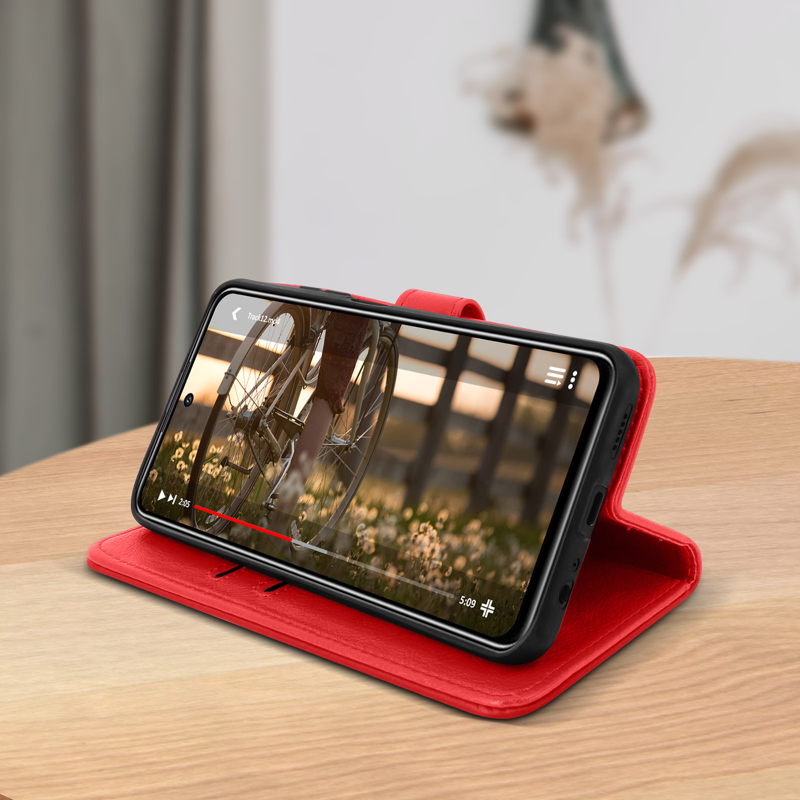 Telefono in custodia rossa, riproduce un video su un tavolo di legno.