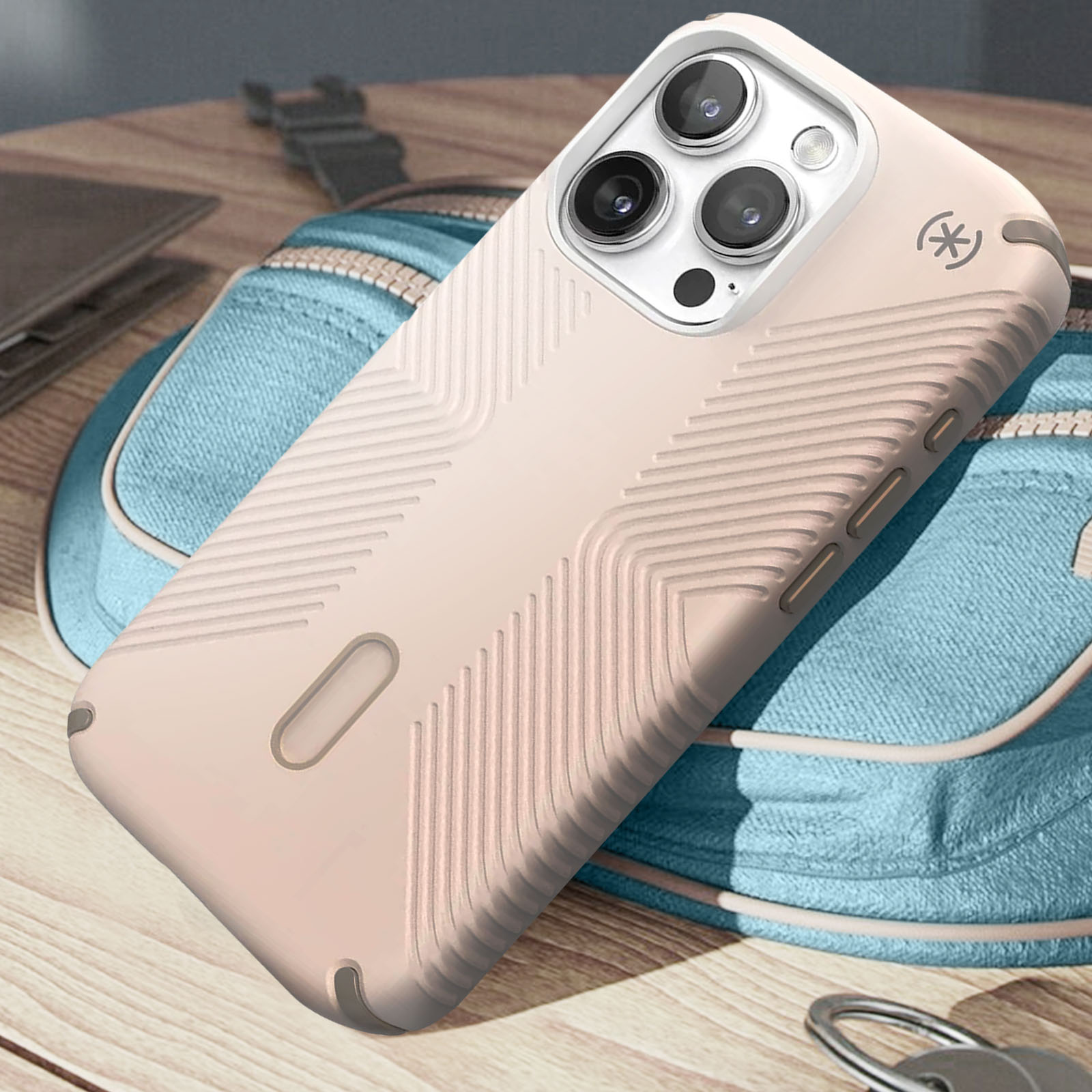 Un étui de téléphone rose, avec un motif texturé, placé sur un sac et une surface en bois.