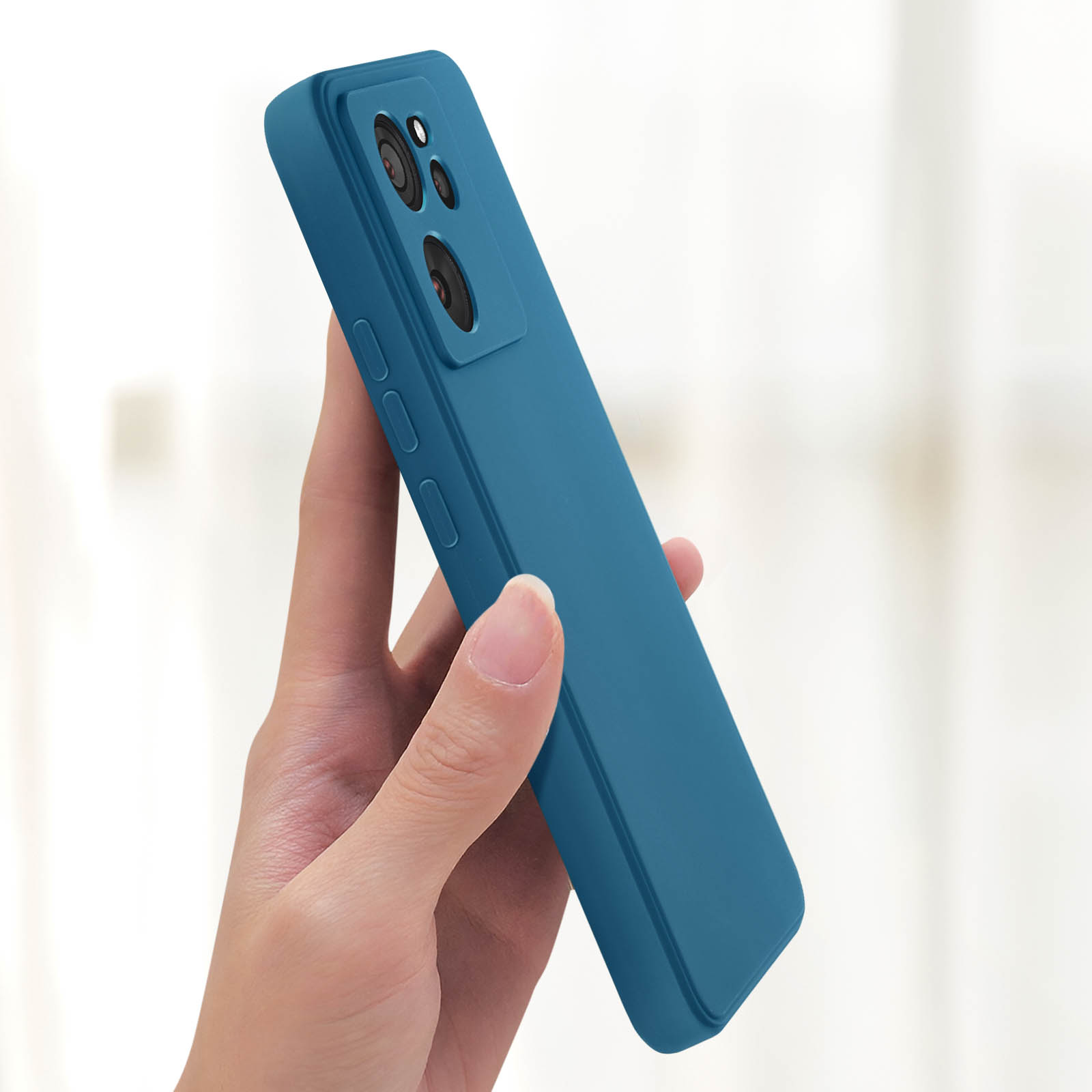 Mano che tiene la custodia blu del telefono. La custodia ha tre fotocamere. Sfondo bianco.