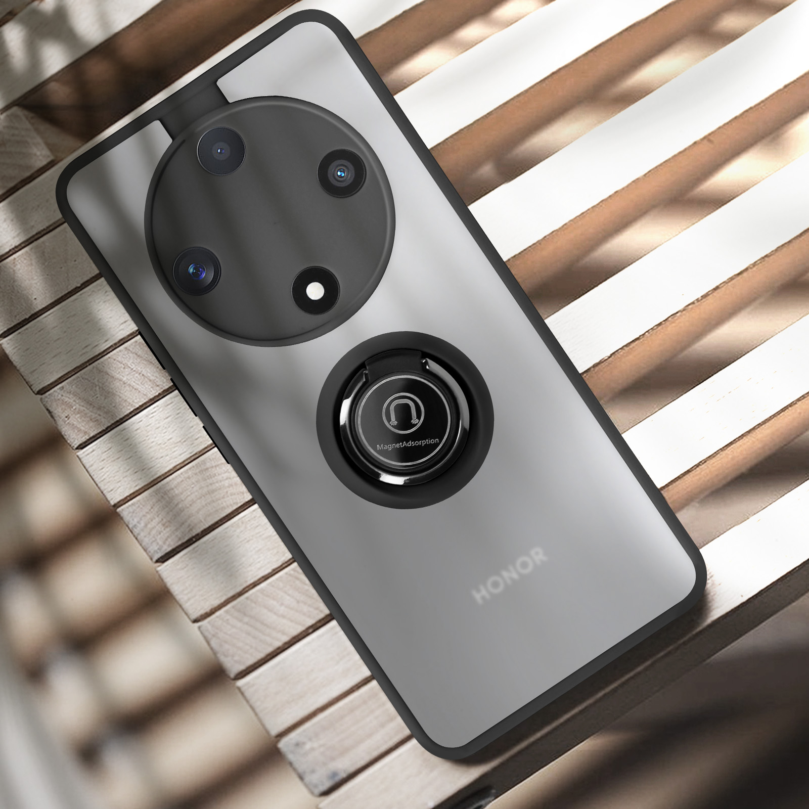 Telefono argentato con protuberanza della fotocamera nera e supporto ad anello. Su una superficie a doghe di legno. Logo HONOR visibile.