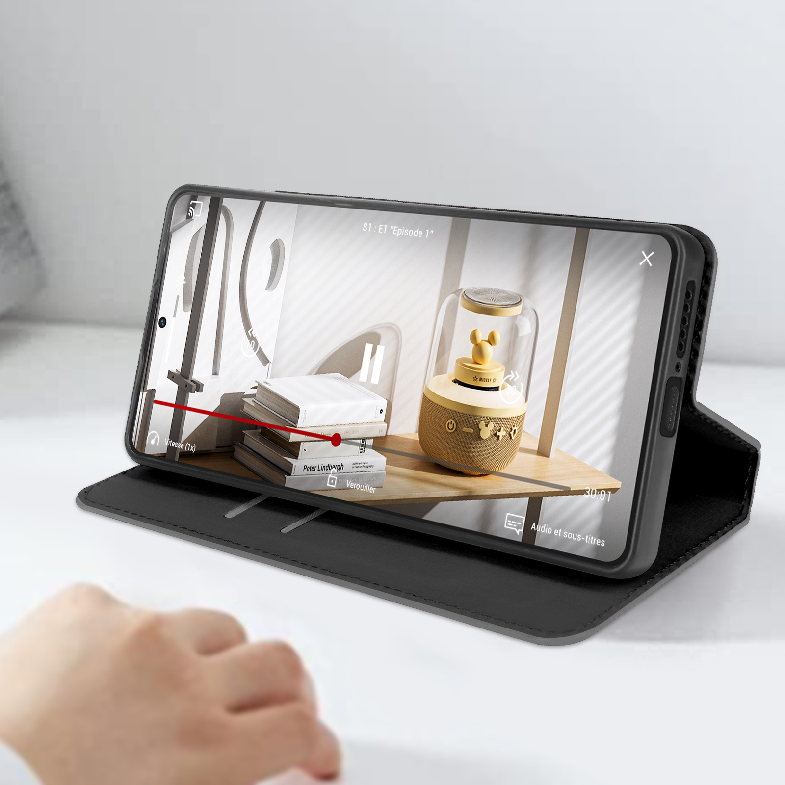 Telefono che mostra un video su un tavolo, con una mano in primo piano. Nera.