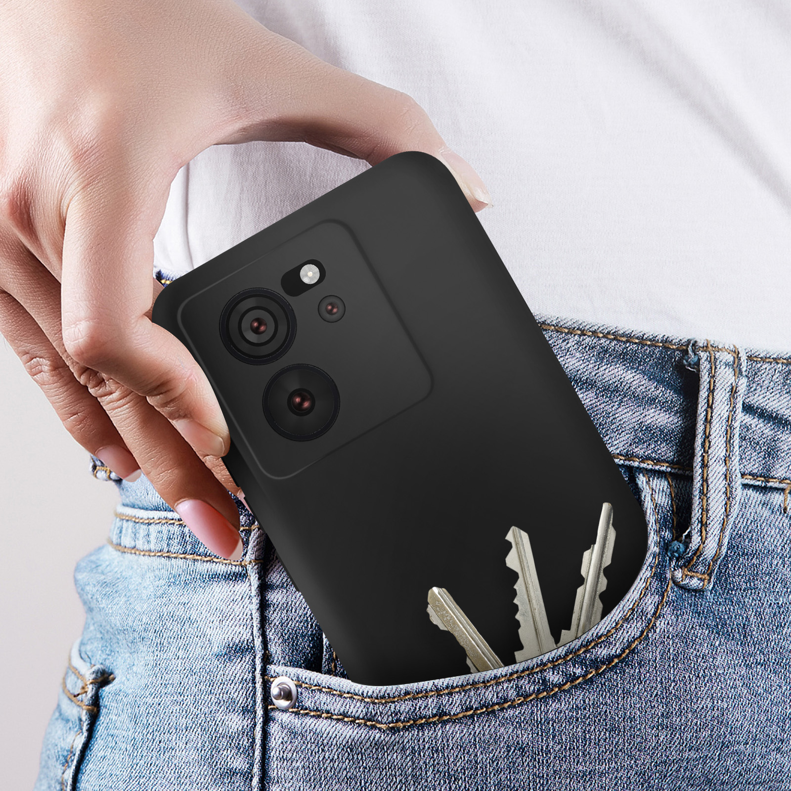 Mano nella tasca dei jeans, che tiene una custodia nera per telefono con tre chiavi in tasca.