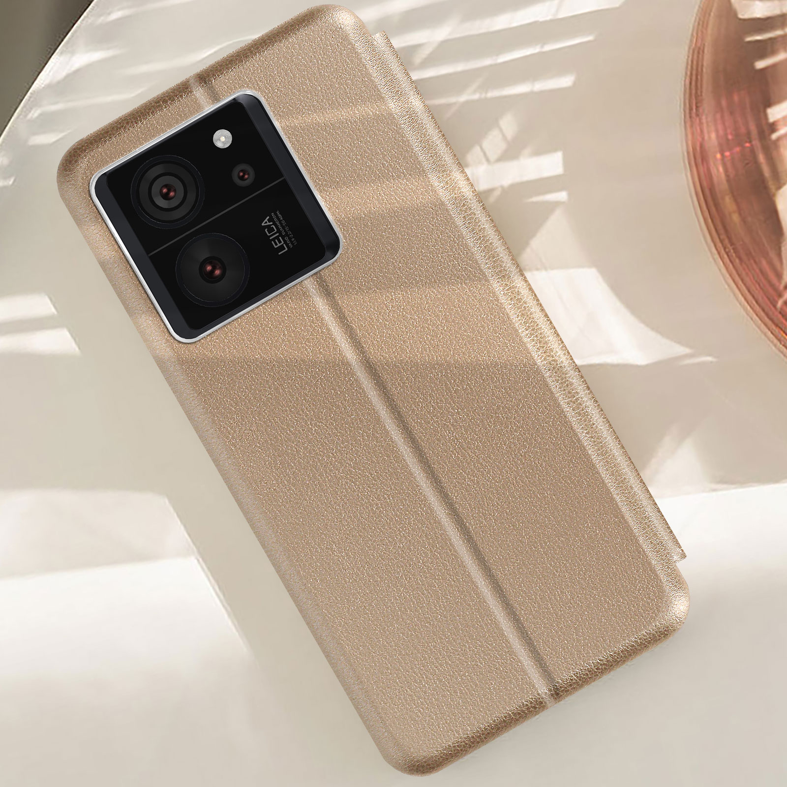 Una custodia per telefono dorata è aperta, mostrando il telefono. Il telefono ha fotocamere e il logo Leica.
