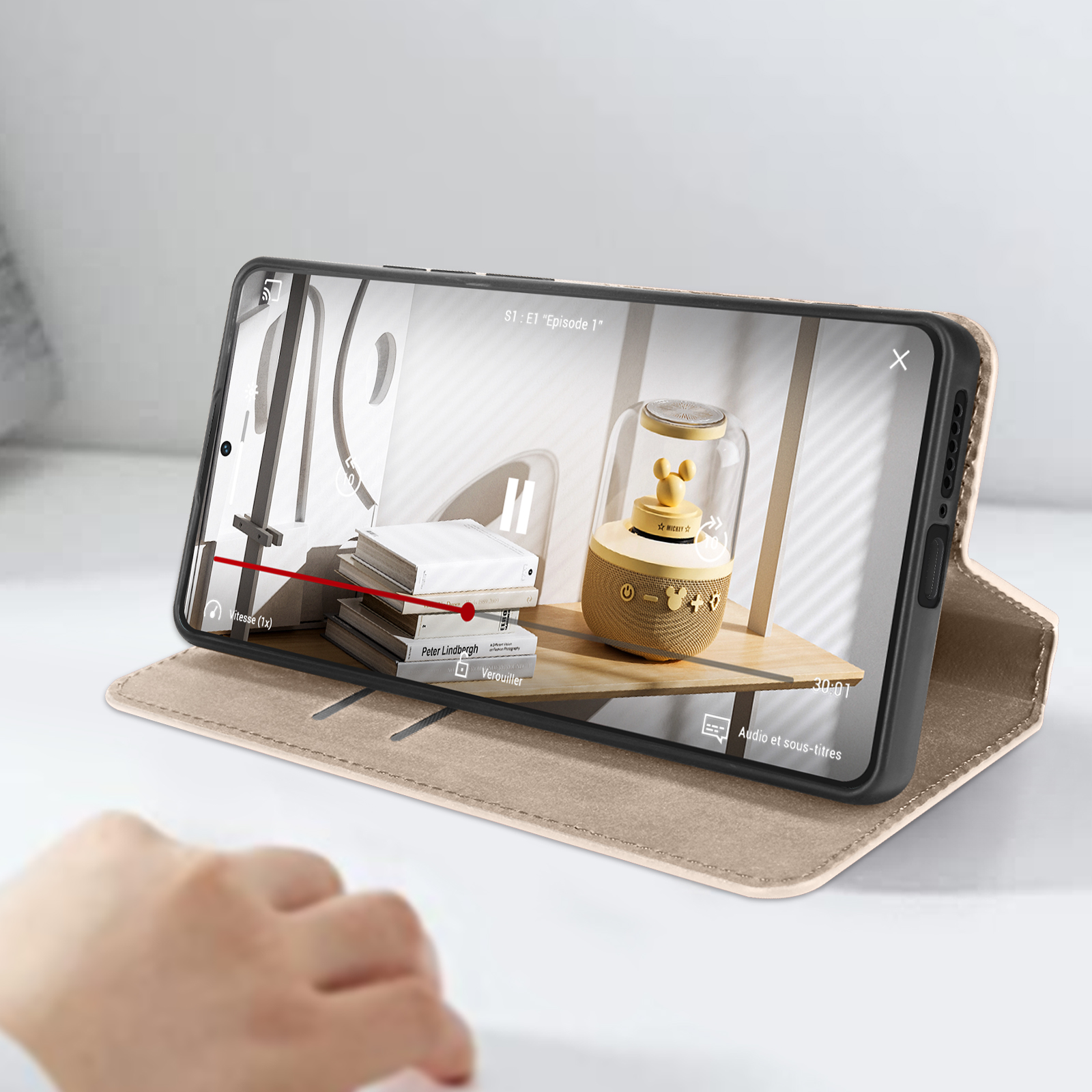 Un telefono aperto mostra un video su un supporto, mano parzialmente visibile.