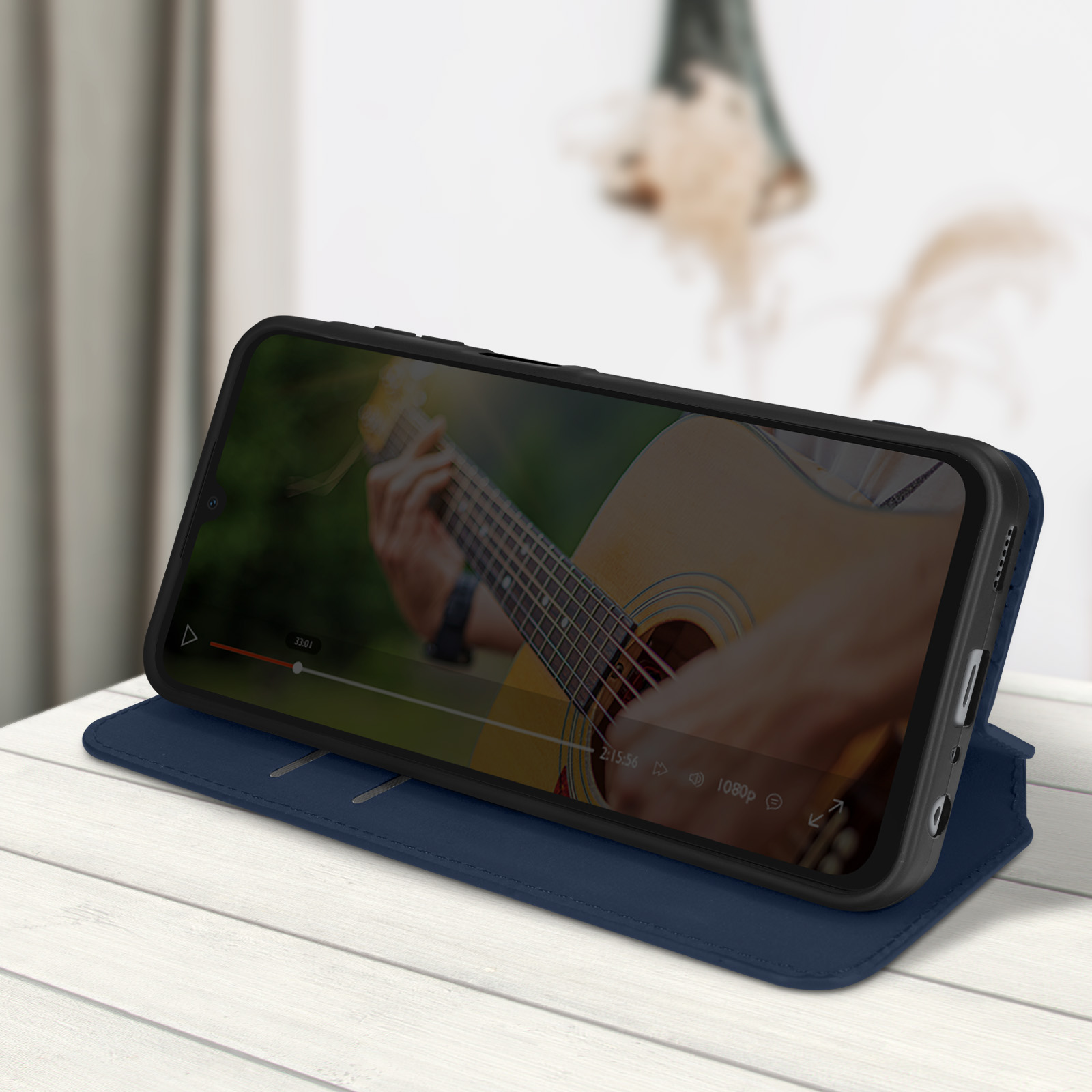 Smartphone in einem Etui, das ein Gitarrenunterrichtsvideo zeigt. Das Telefon liegt auf einem blauen Etui auf einem weißen Holztisch.