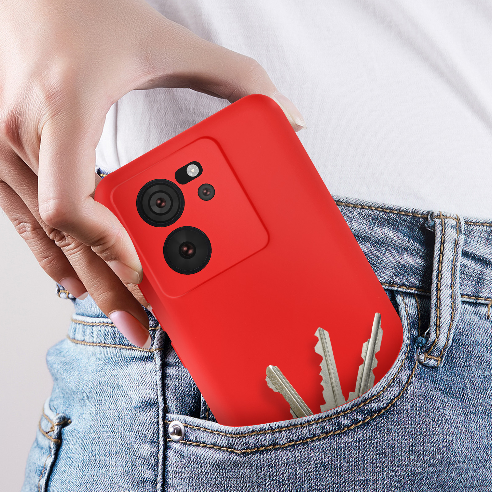 Een hand houdt een rode telefoonhoes in een zak met sleutels. Jeans achtergrond.