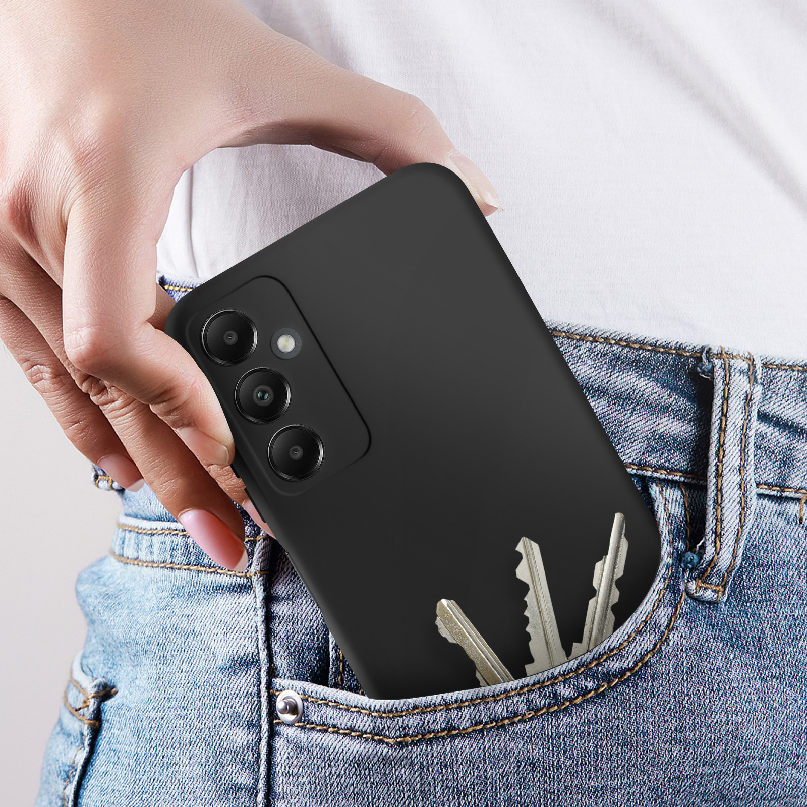 Mano in tasca di jeans che tiene un telefono nero e chiavi. Sfondo camicia bianca.