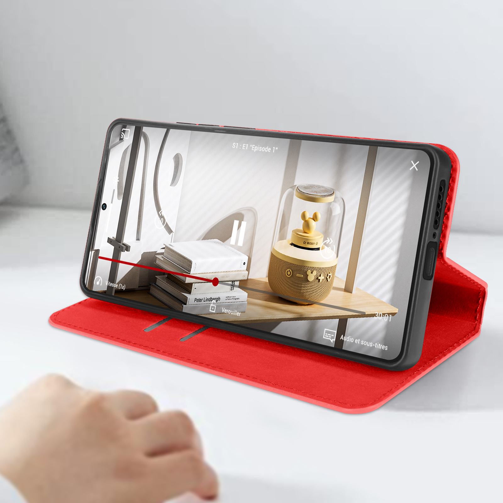 Telefono in custodia rossa che mostra un video, con una mano in primo piano.