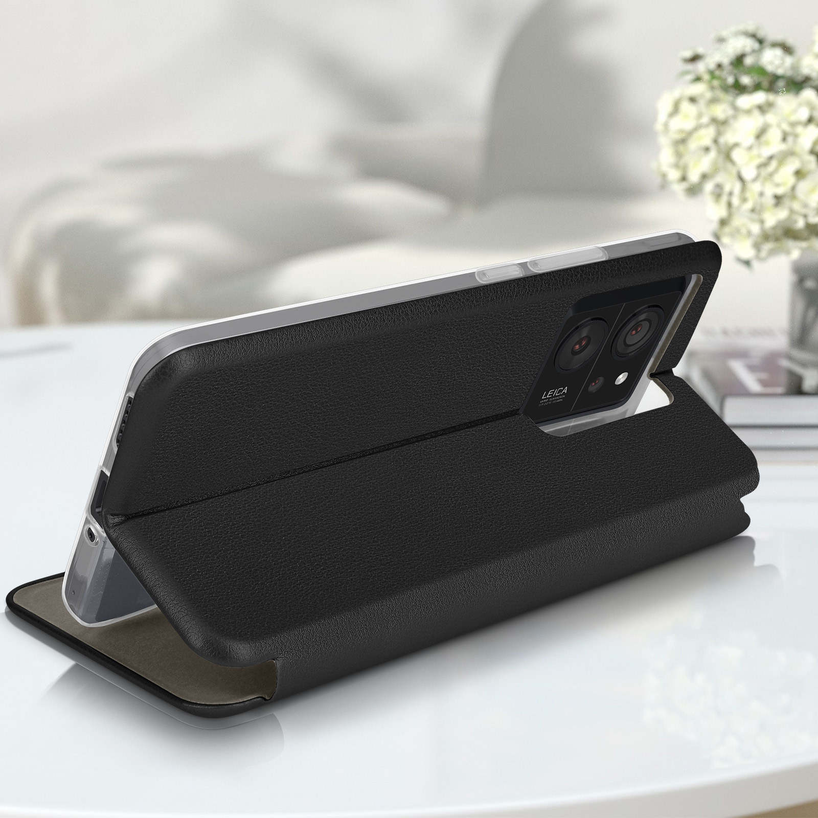 Custodia in pelle nera, aperta, con telefono dentro. Tavolo bianco, sfondo sfocato.