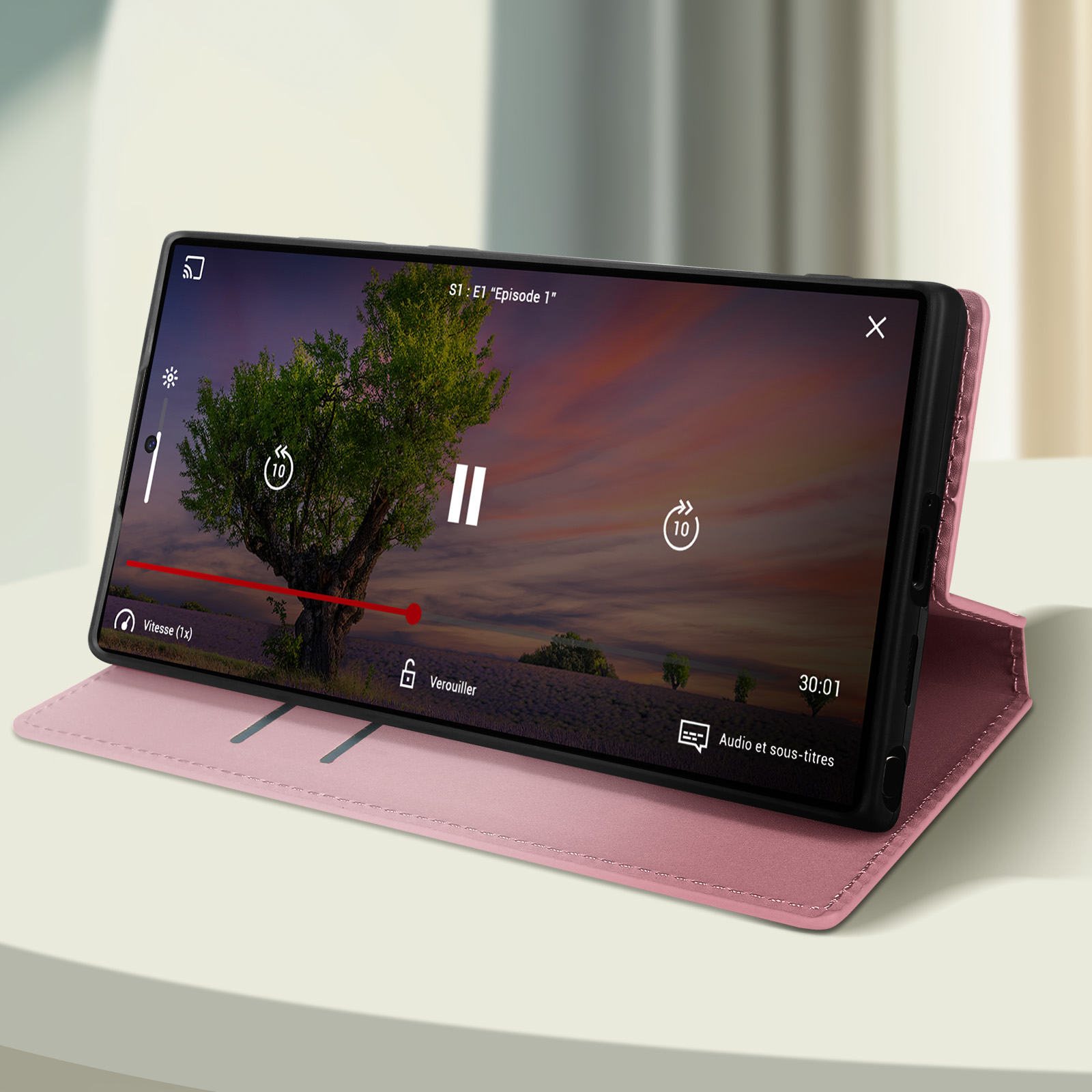 Un telefono in una custodia rosa mostra un video di un albero. La custodia è su una superficie bianca.