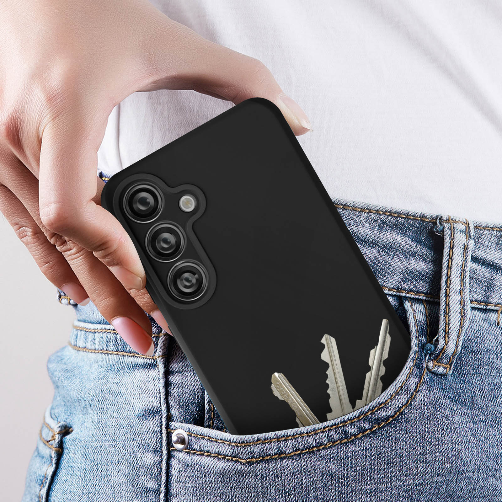 La mano di una persona in una tasca dei jeans che tiene una custodia nera per telefono con le chiavi. Le chiavi sono parzialmente visibili.