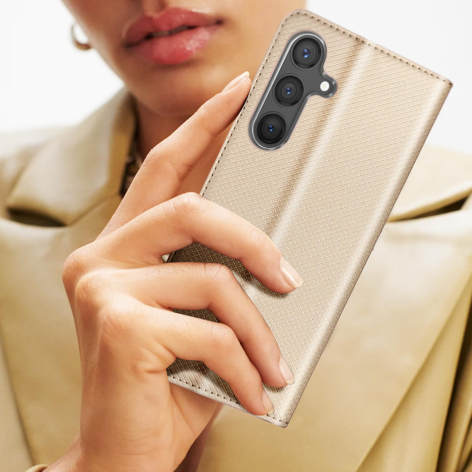 La mano di una donna che tiene una custodia per telefono dorata e strutturata. Il telefono ha tre fotocamere. Lo sfondo è sfocato.
