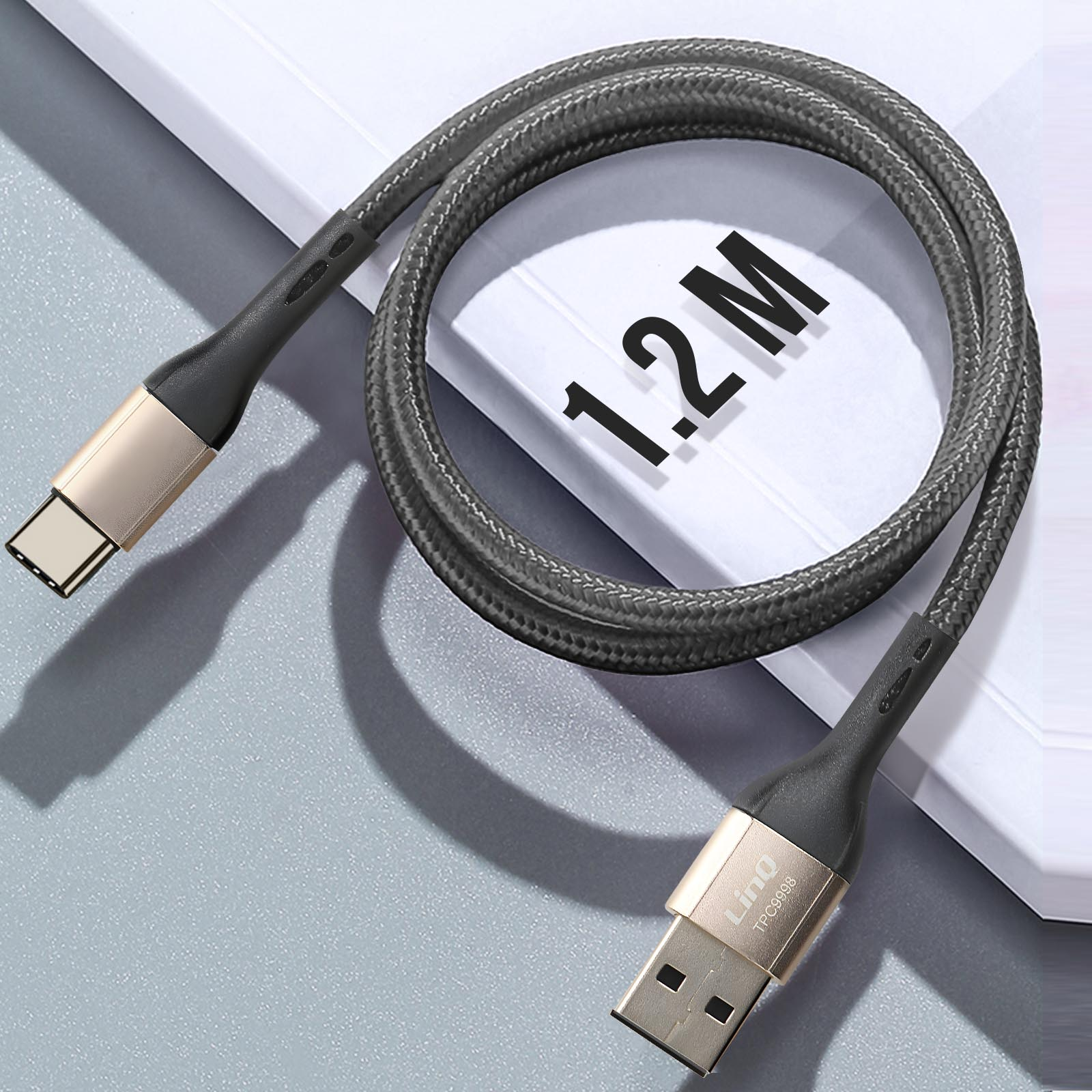 Cavo USB-C a USB intrecciato, grigio con connettori dorati, su una superficie chiara.