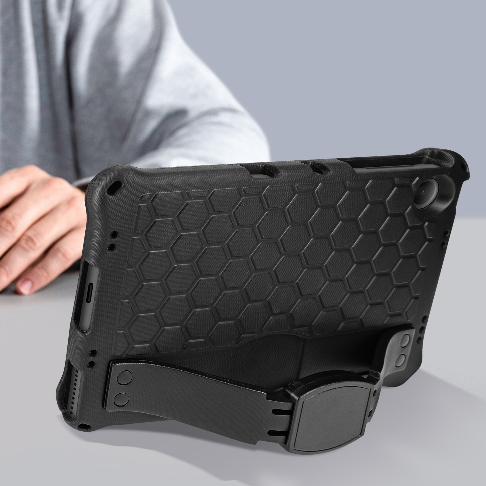 Schwarzes Tablet in einer robusten Hülle mit Ständer. Arme einer Person im Hintergrund.