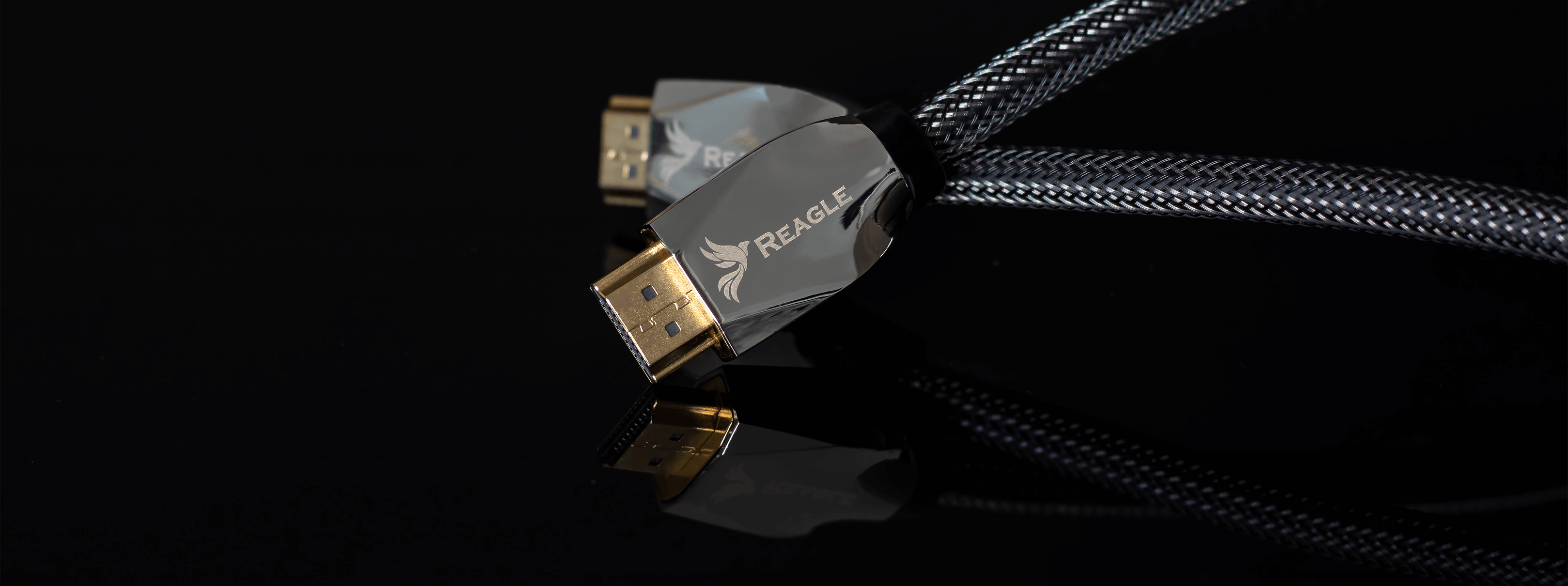 Zbliżenie dwóch czarnych kabli HDMI ze złotymi złączami. Kable odbijają światło na czarnej powierzchni, z logo.