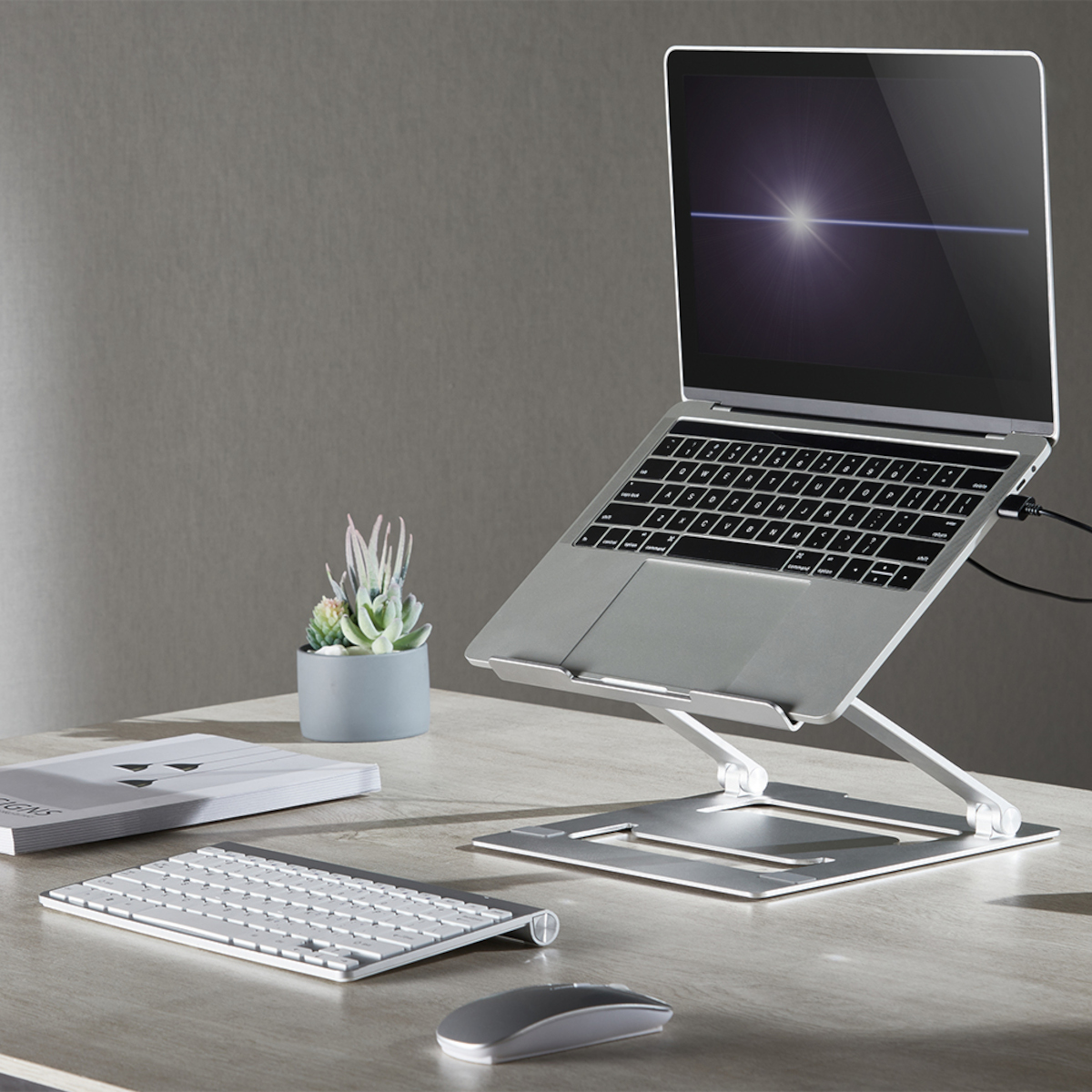 Ein Laptop auf einem silbernen Laptopständer. Tastatur und Maus auf dem Schreibtisch.
