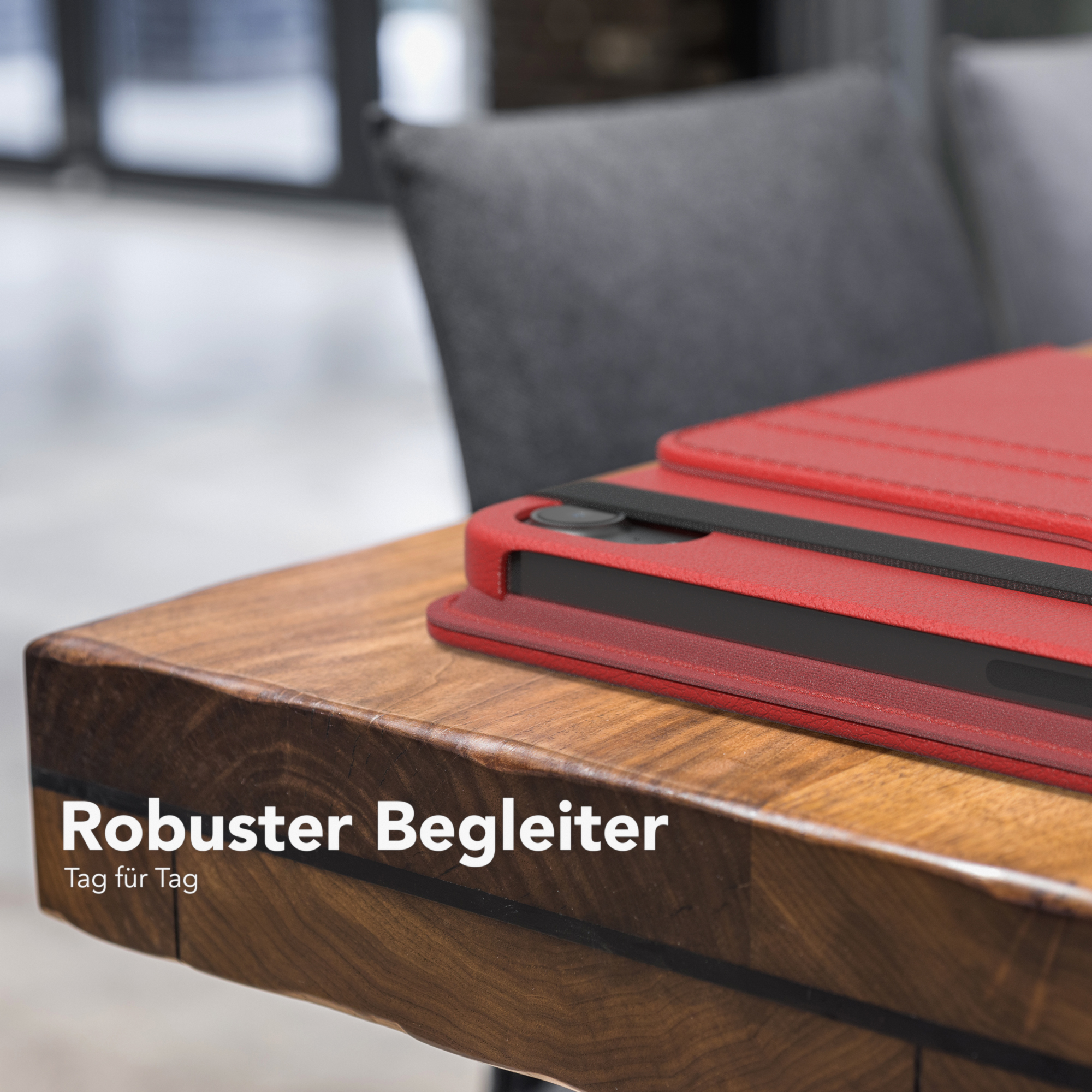Rote Tablethülle auf einem Holztisch. Schwarzer Riemen über der Hülle.